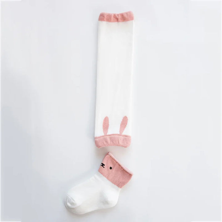 White baby leg warmer with pink trim and bunny-ear details beside a white sock with a pink animal-face cuff.