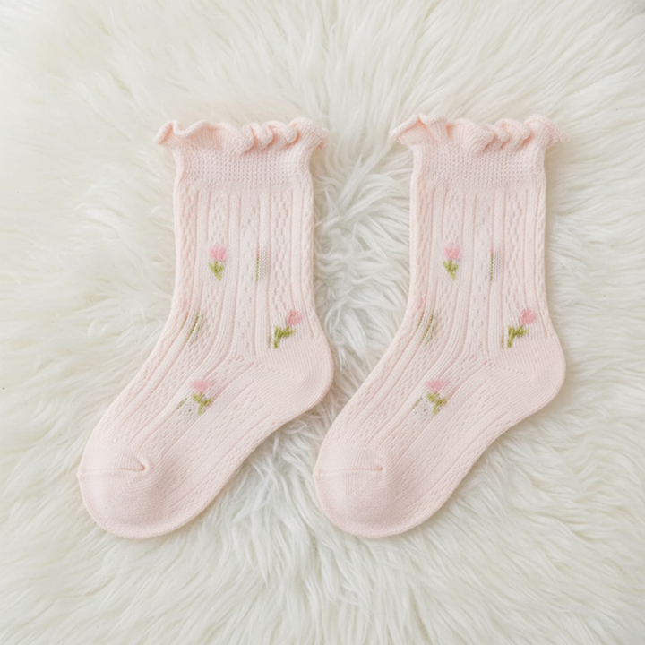 Pair of pink baby socks with floral details and ruffled cuffs on a fluffy white surface.