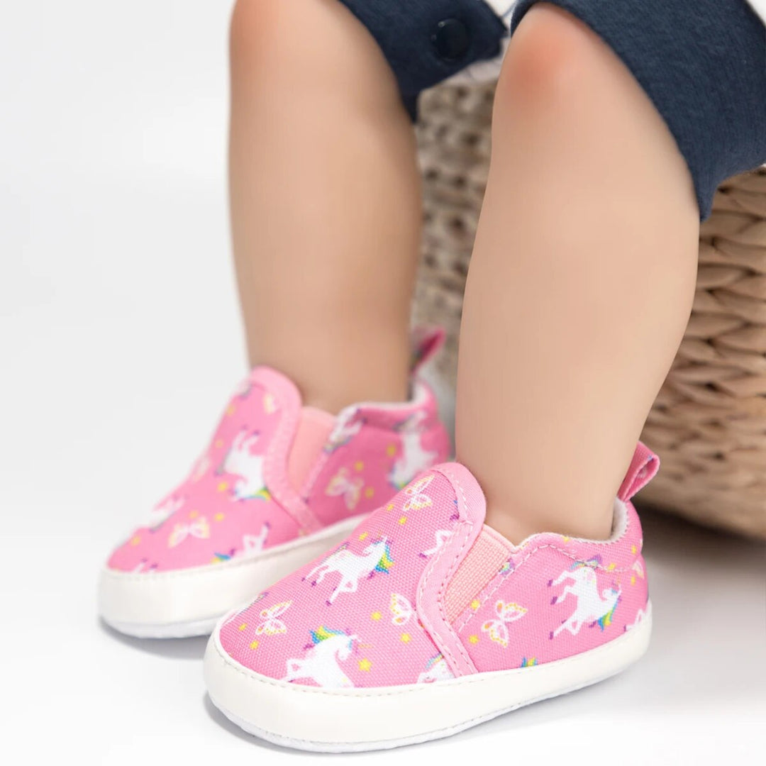 Pink unicorn-print baby slip-on sneakers with white soles, shown on feet