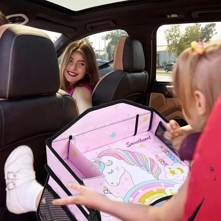 Child using a pink unicorn-print travel tray in the back seat of a car