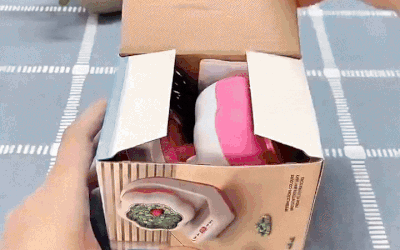 Hands opening a box containing the pink-and-white electric beading machine.