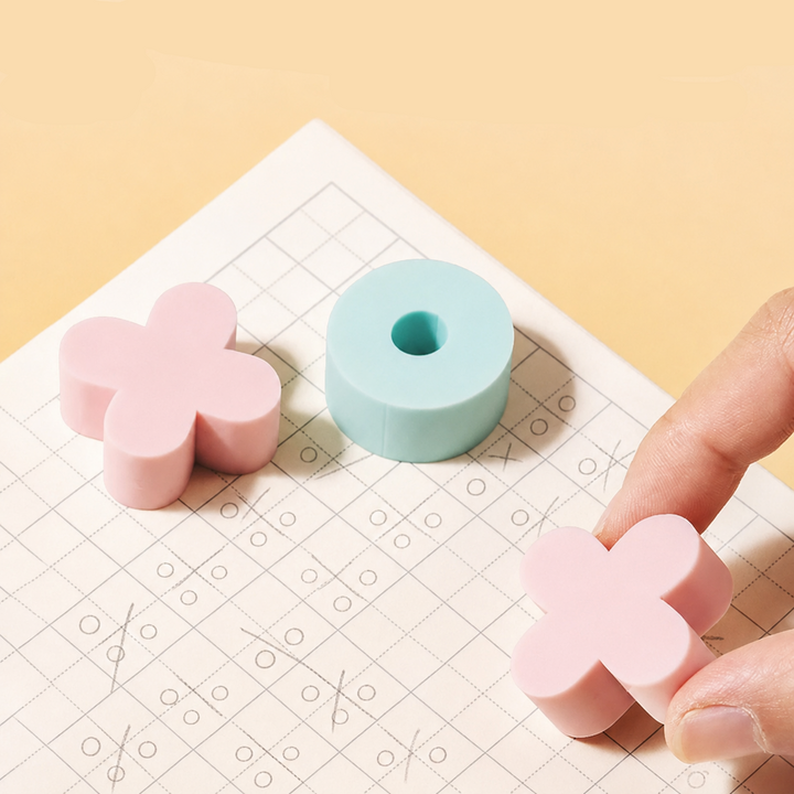 Pink X and mint O erasers on pencil-marked grid paper.