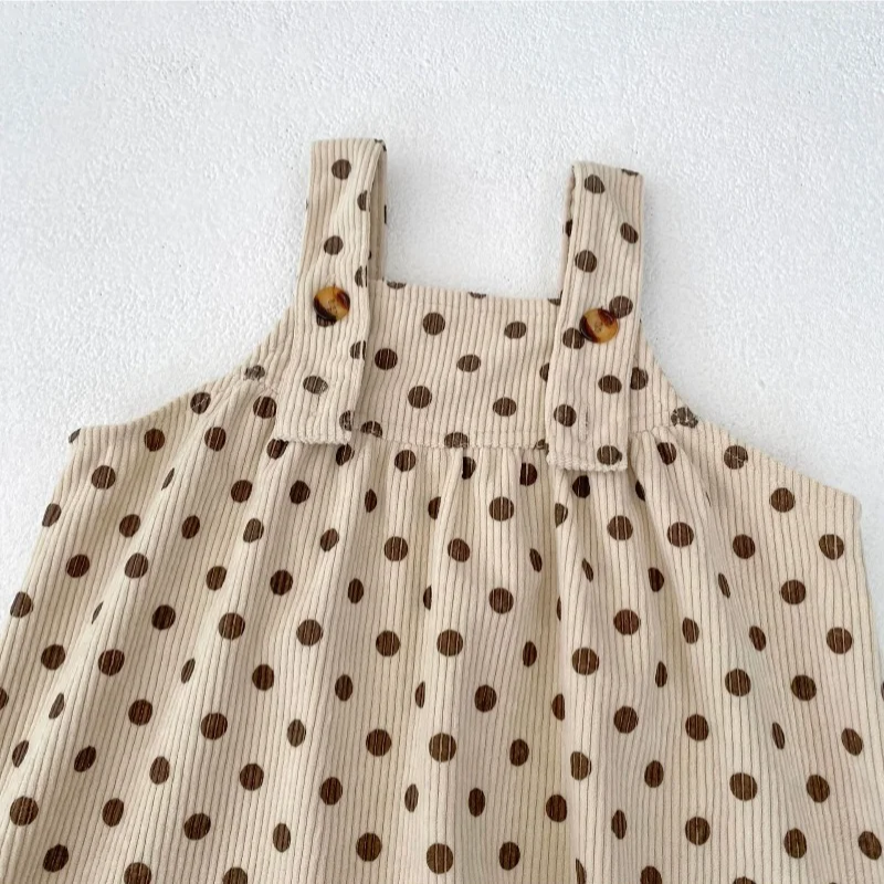 Close-up of buttoned shoulder straps and gathered fabric on the apricot polka-dot jumpsuit.