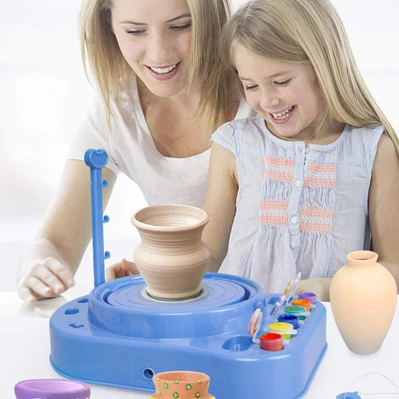 Adult and child beside a blue pottery wheel with a clay vase and paint pots