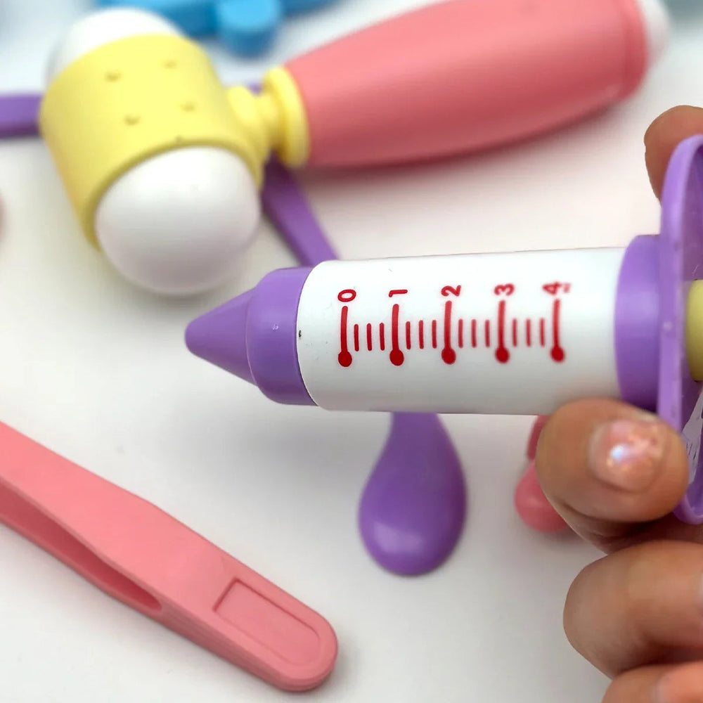 Close-up of a toy syringe with a purple tip and plunger beside a pink-and-yellow reflex hammer