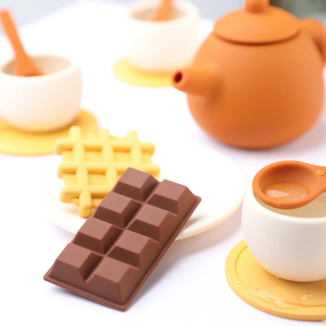 Silicone waffle and chocolate-bar play pieces beside cups and an orange toy teapot