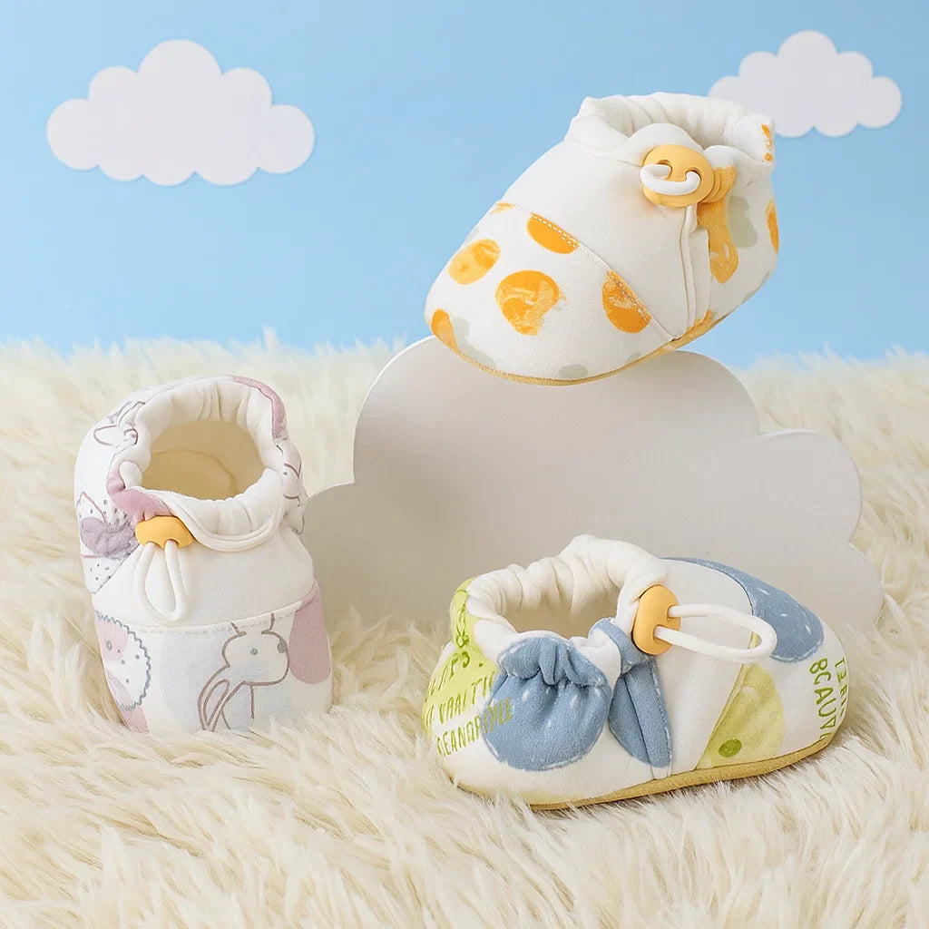 Printed baby shoes with elastic openings displayed on a soft rug against a cloud backdrop