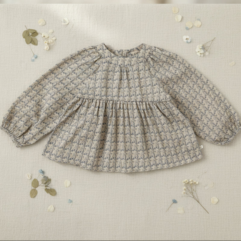Printed long-sleeve blouse with a gathered neckline displayed on fabric with floral accents