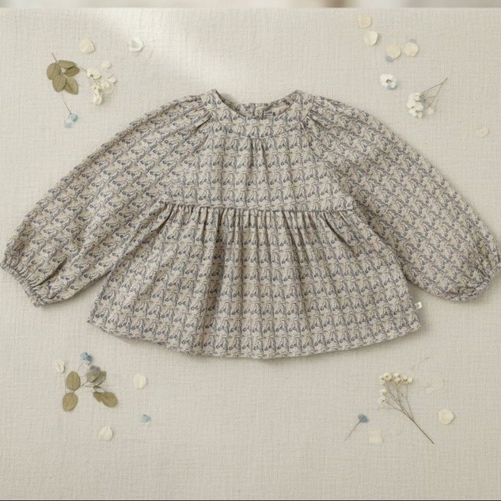 Printed long-sleeve blouse with a gathered neckline displayed on fabric with floral accents