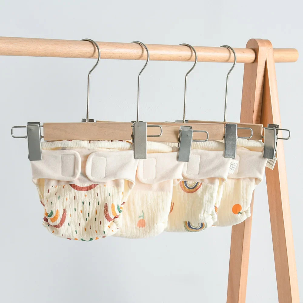 Printed cloth diapers with wide waistbands hanging from clips on a wooden rack