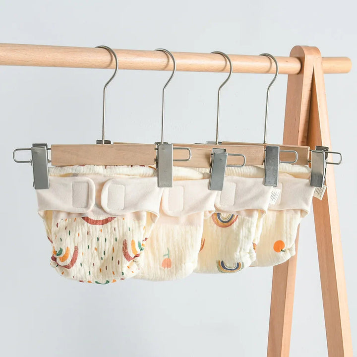 Printed cloth diapers with wide waistbands hanging from clips on a wooden rack