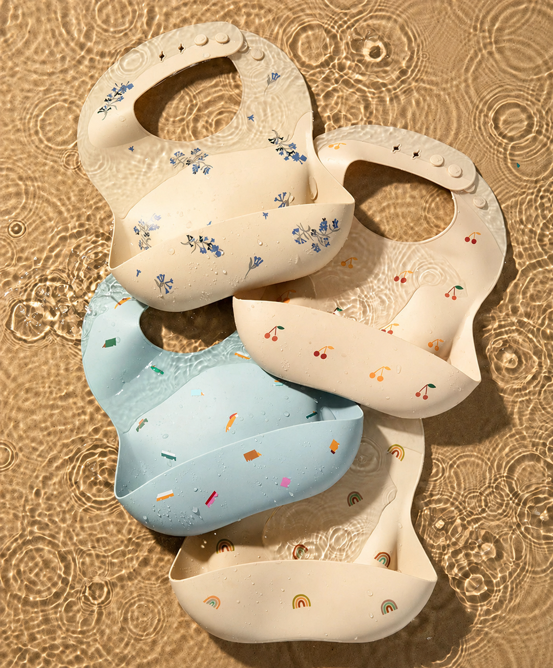 Blue and cream printed silicone bibs with adjustable neck fasteners on textured fabric