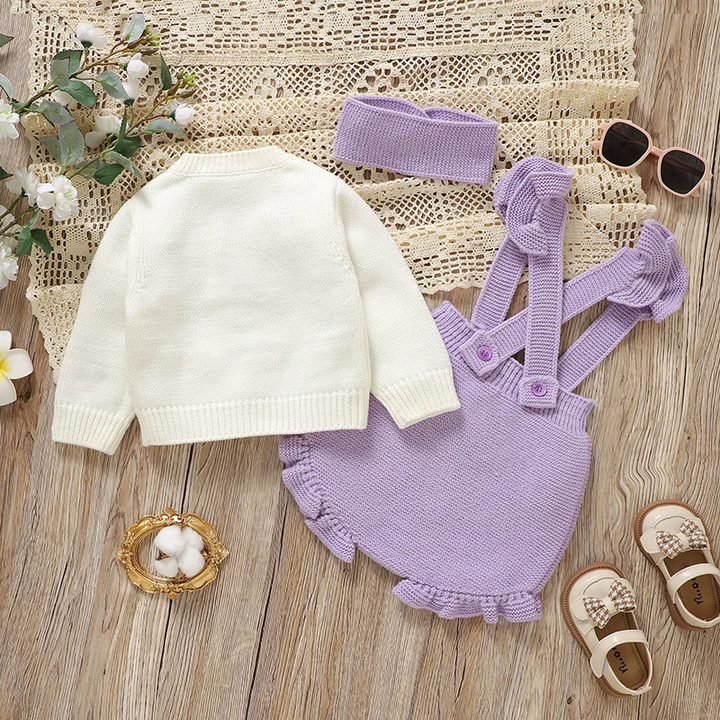 Back of the white knit cardigan beside purple overalls and a coordinating headband