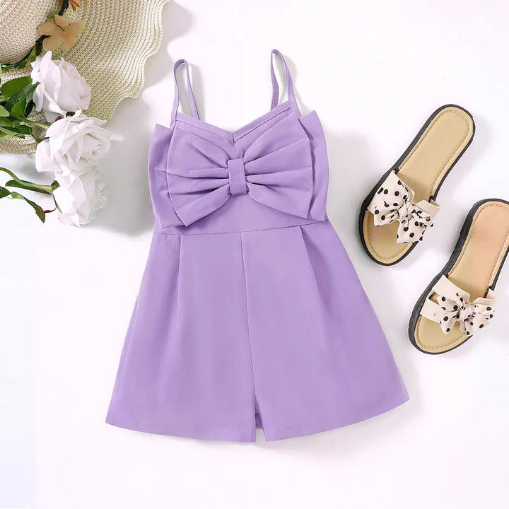 Purple bow-front romper styled beside sandals, white flowers and a straw hat