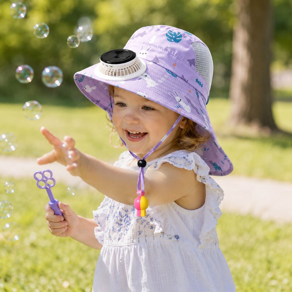 Child wearing a purple fan hat while playing with bubbles outdoors.