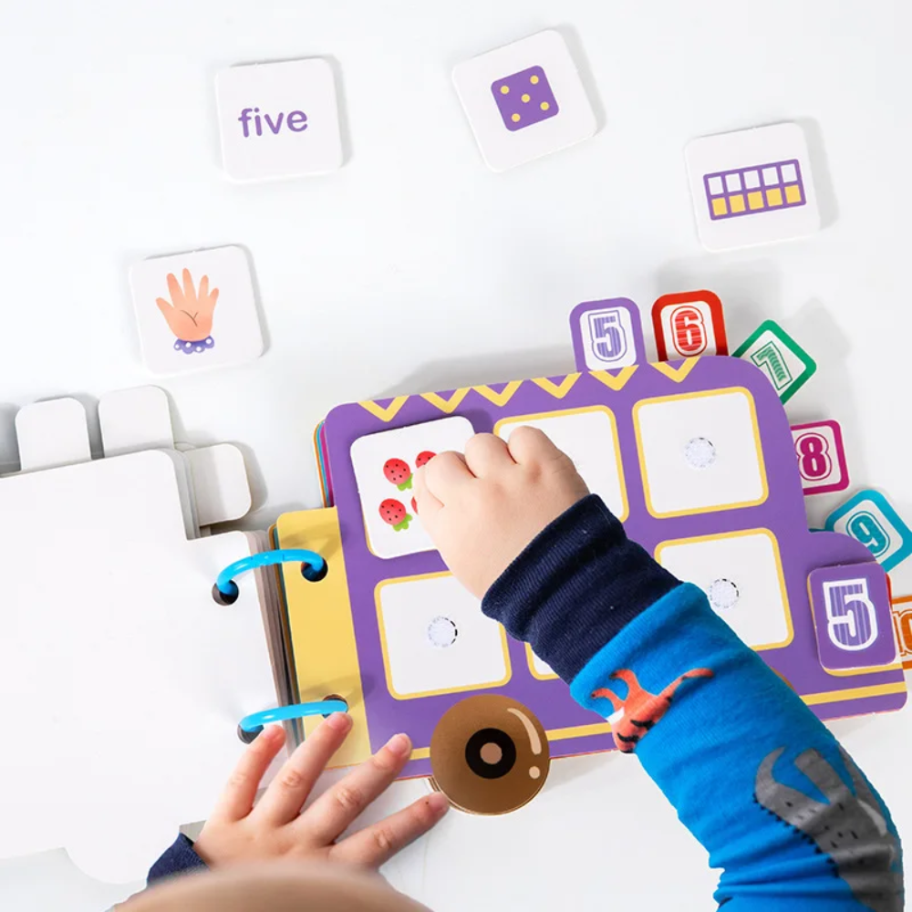 Hands matching a picture tile on the purple number-five page, with loose counting tiles nearby.