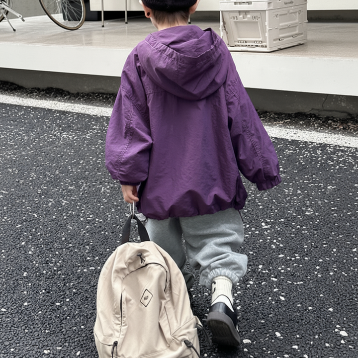 Rear view of a child wearing a purple windbreaker with the hood down outdoors