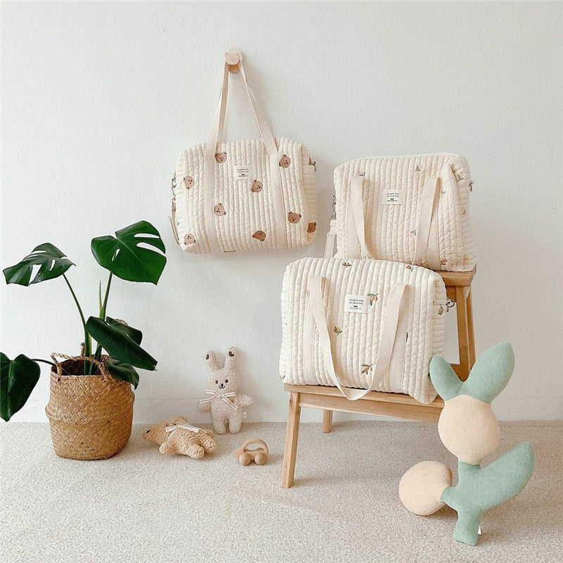 Three cream quilted diaper bags with small prints displayed on a wall and wooden chair