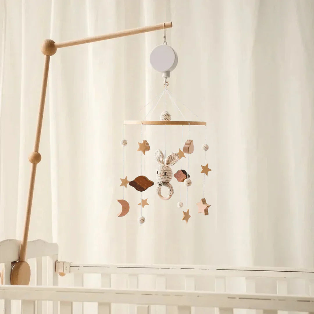 Rabbit baby mobile with moon and star shapes displayed on a wooden arm in a nursery