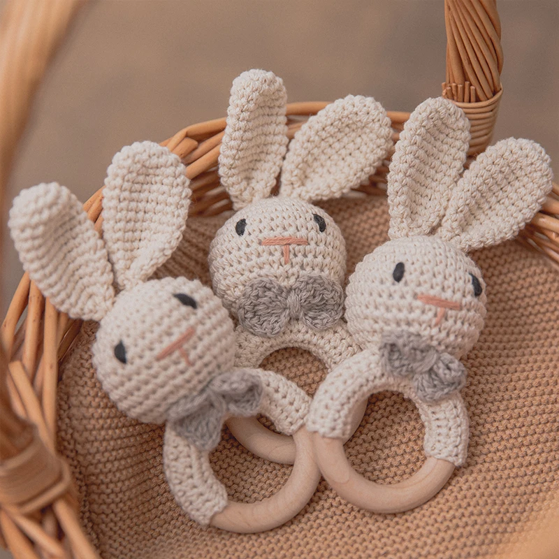 Three crocheted rabbit rattles with wooden rings in a woven basket