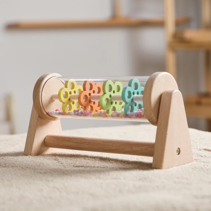 Front view of the wooden rain sound toy with colorful wheels and beads on a rug.