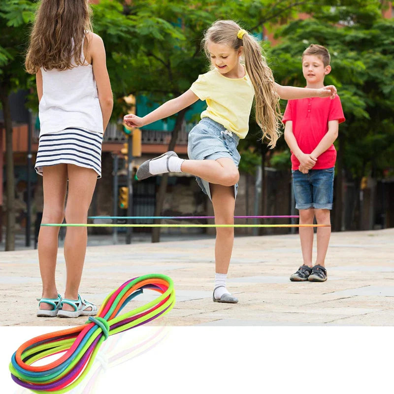 Children playing a jumping game outdoors with a rainbow elastic band