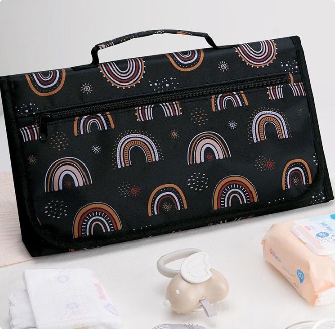 Folded black changing mat with rainbow print, carry handle, and front zip pocket.