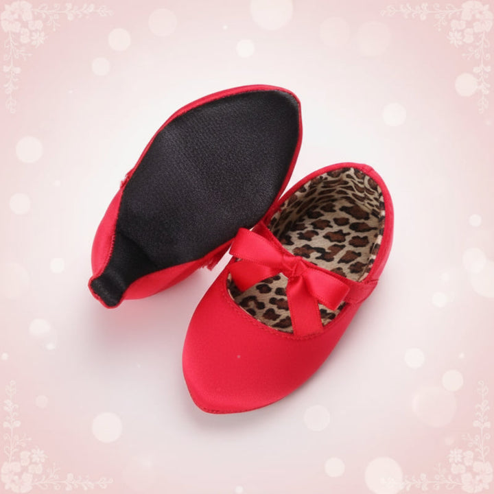 Red baby dress shoes showing a black sole, leopard-print lining, and ribbon bow