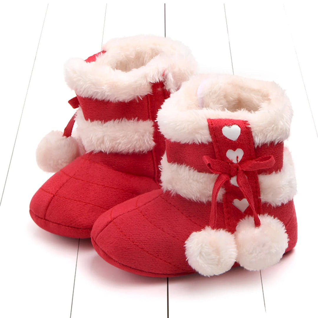 Red baby snow boots with cream trim, heart accents, bows, and dangling pom-poms