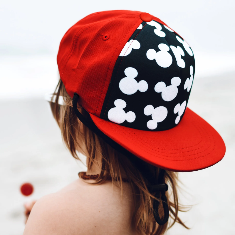 Child wearing a red and black cap with a white silhouette pattern and flat red brim