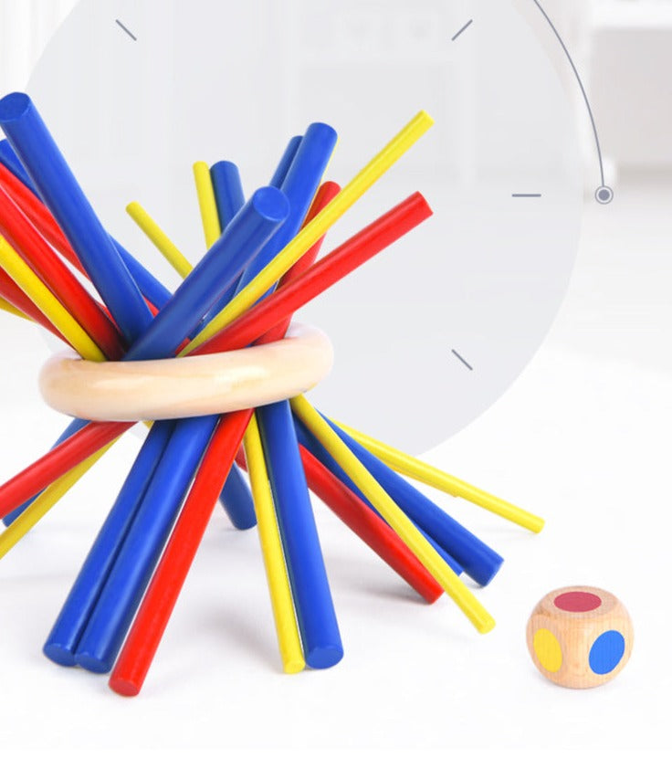 Red, blue, and yellow sticks balanced inside a wooden ring beside a color-marked die.