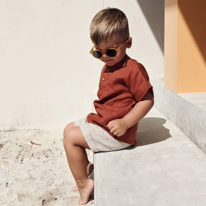 Boy sitting on a step in the red button-detail shirt and light shorts