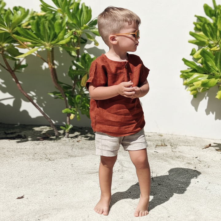 Boy wearing a red cotton-linen shirt, light shorts, and sunglasses outside
