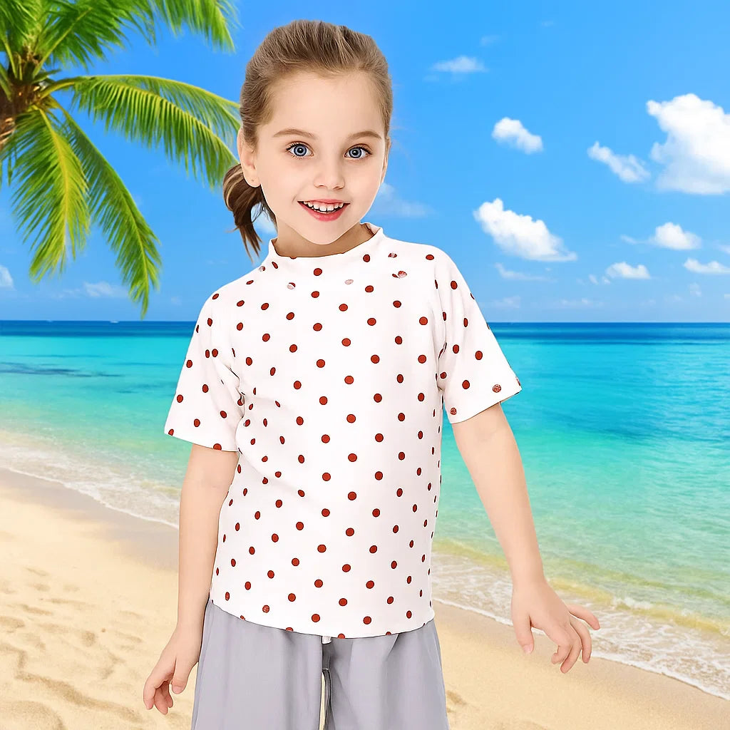Child wearing a white swim shirt with red dots beside the ocean
