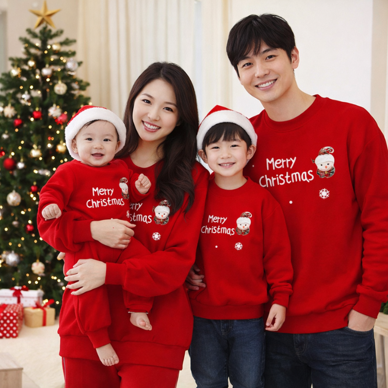 Family wearing matching red Christmas sweaters and a baby romper beside a decorated tree