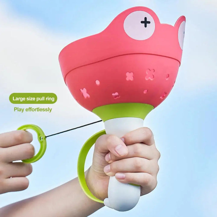 Hands holding a red frog-shaped launcher and pulling its green ring