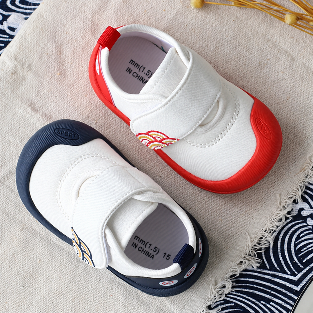 White baby sneakers with red and navy toe caps and wide strap closures