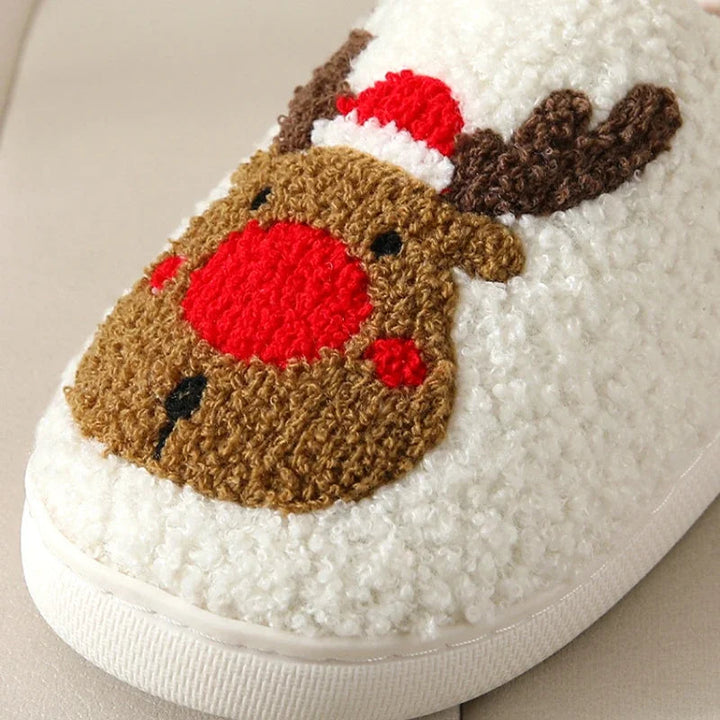 Close-up of a red-nosed reindeer motif on a cream plush slipper.