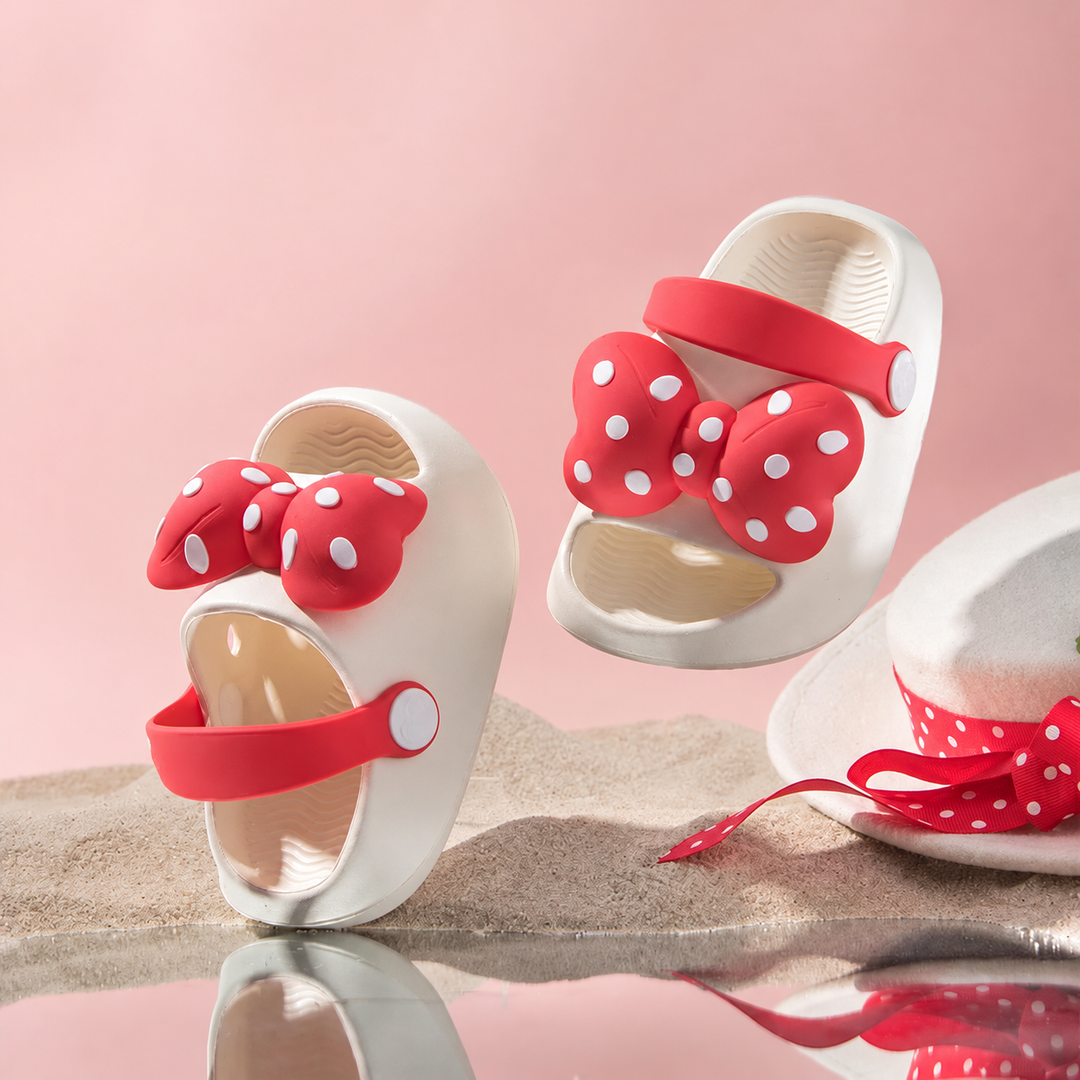 White kids' sandals with red polka-dot bows and matching straps on a beach-themed display