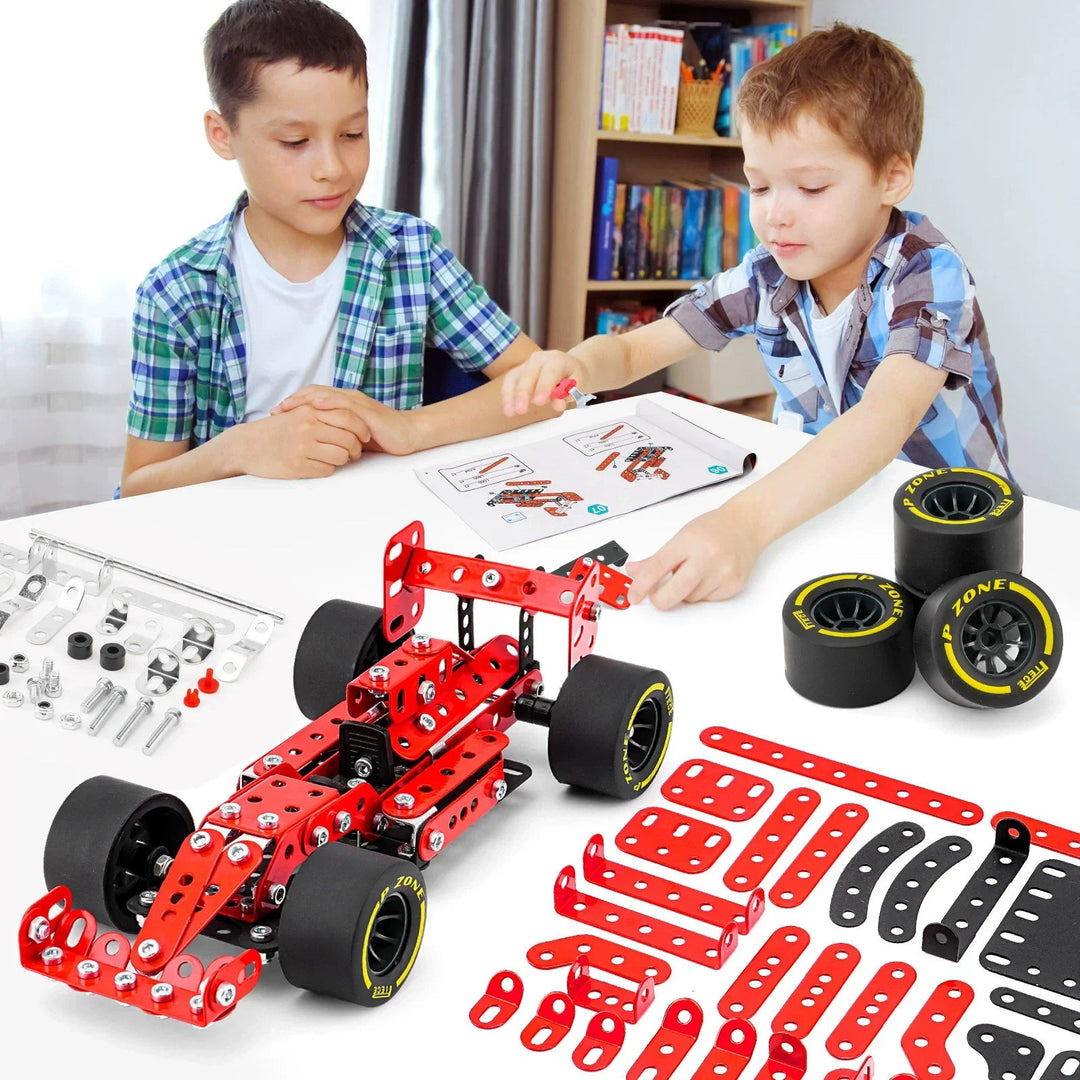 Two children building a red racing car with instructions, loose parts, wheels, and tools