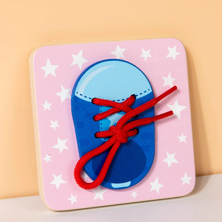 Shoelace practice busy board with a blue shoe and red laces on a pink star-patterned background.