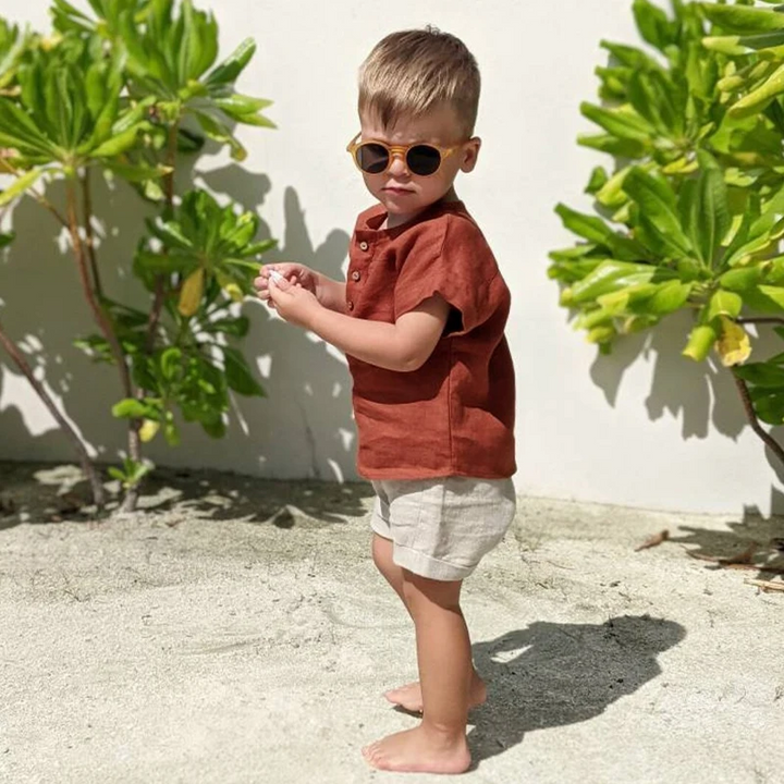 Boy standing outdoors in the red short-sleeve shirt with light shorts