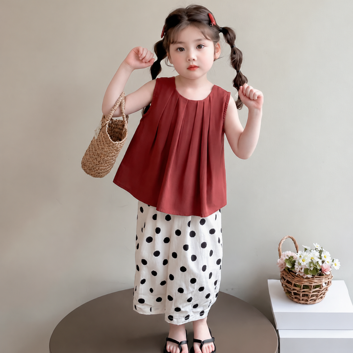 Child wearing a red sleeveless top and white pants with black polka dots