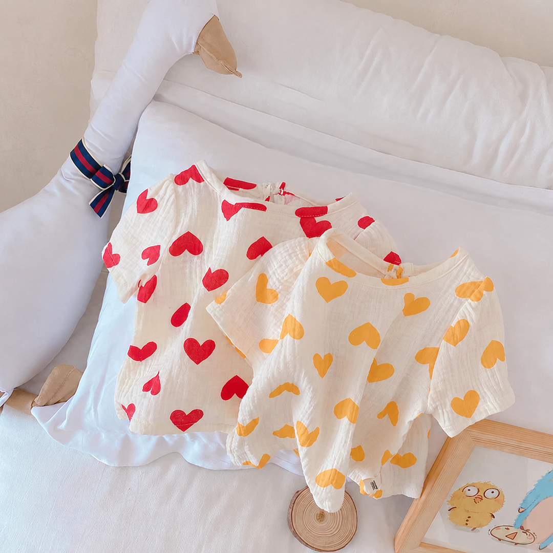 Red and yellow heart-print short-sleeve tops displayed together on white bedding