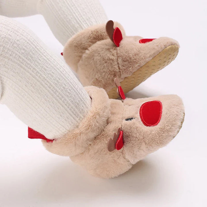 Tan reindeer baby slippers worn with white pants, with one textured sole visible