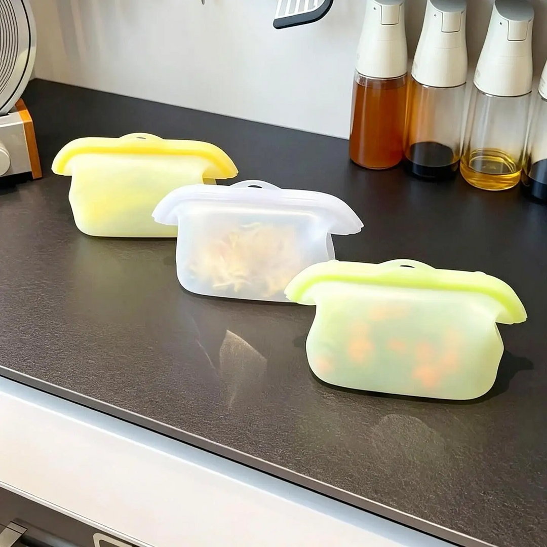 Three reusable silicone food storage bags standing on a kitchen counter.