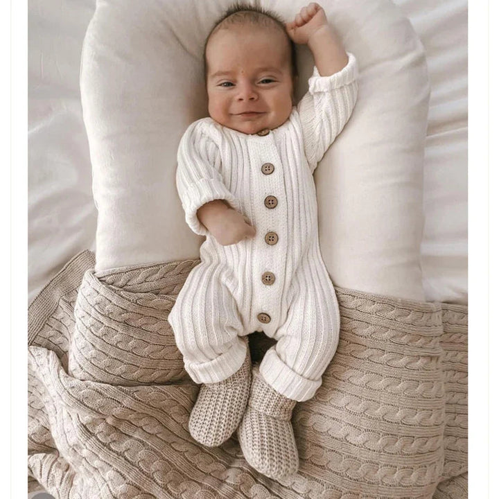 Baby wearing a white long-sleeve knit romper with rolled cuffs and gray knitted booties