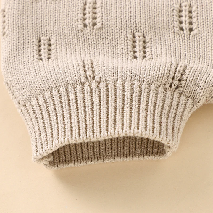 Close-up of an elastic ribbed leg cuff and textured knit on beige baby overalls.
