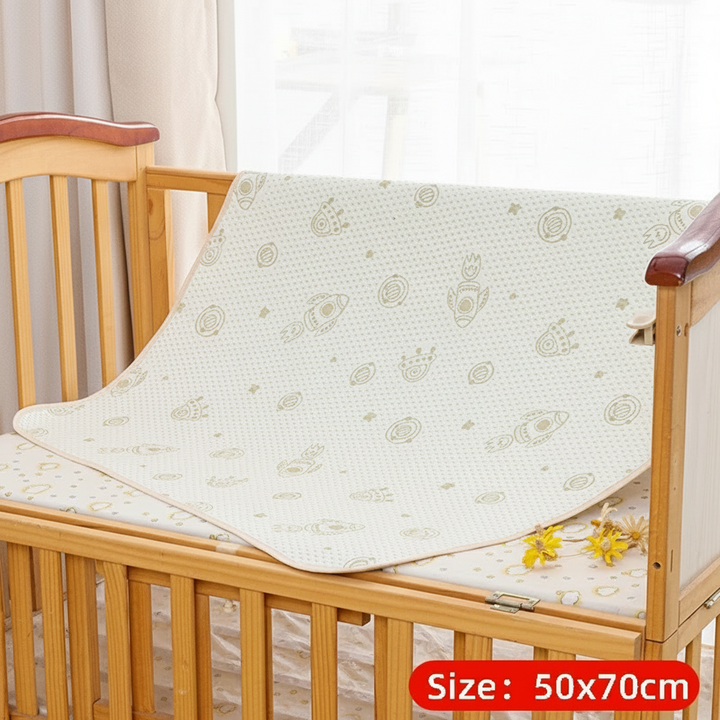 Rocket-print mattress protector labeled 50 x 70 cm draped in a wooden crib
