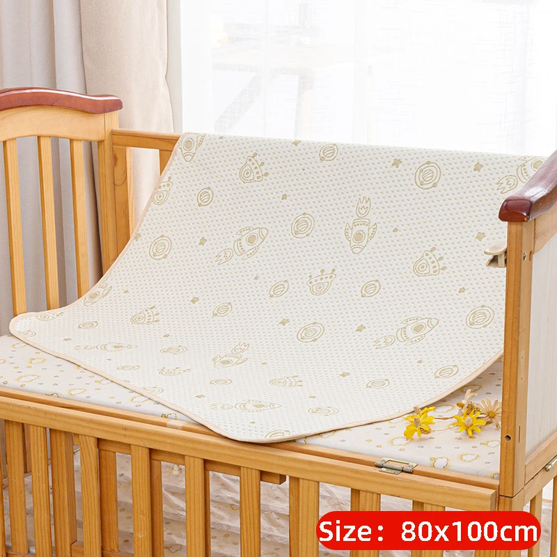 Rocket-print mattress protector labeled 80 x 100 cm draped in a wooden crib